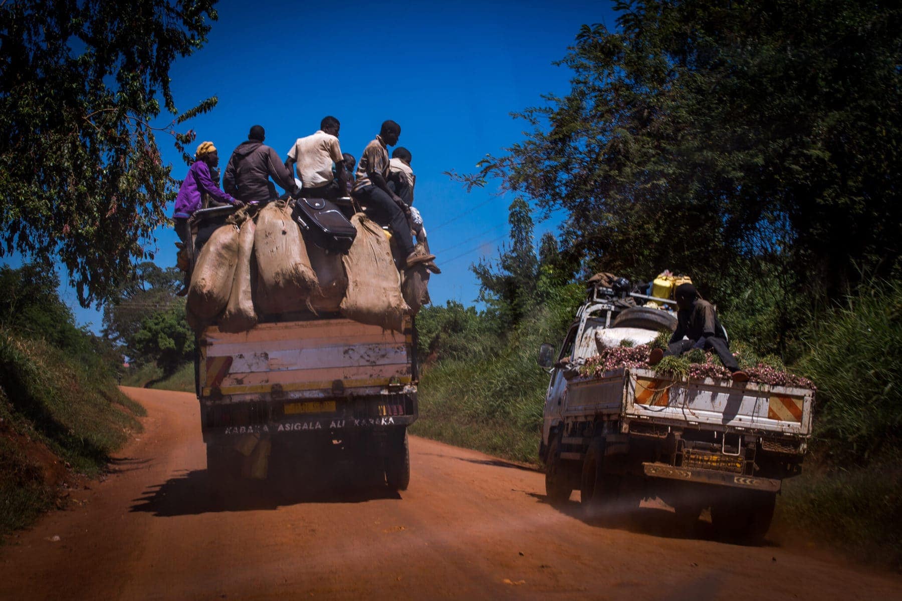 Traffic in Uganda is dangerous. In the picture, a crowded truck overtakes a smaller truck on a dirt narrow road