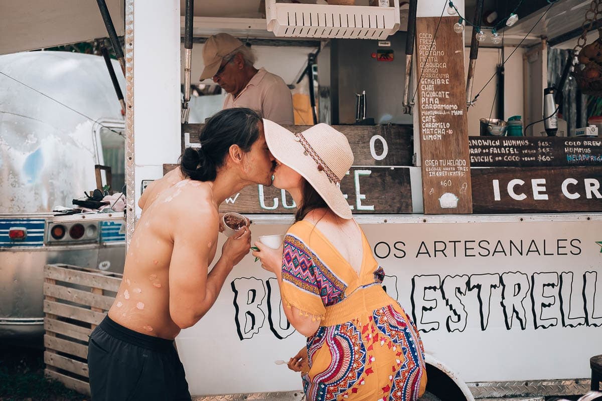 A couple giving each other a kiss and holding an ice cream cone.